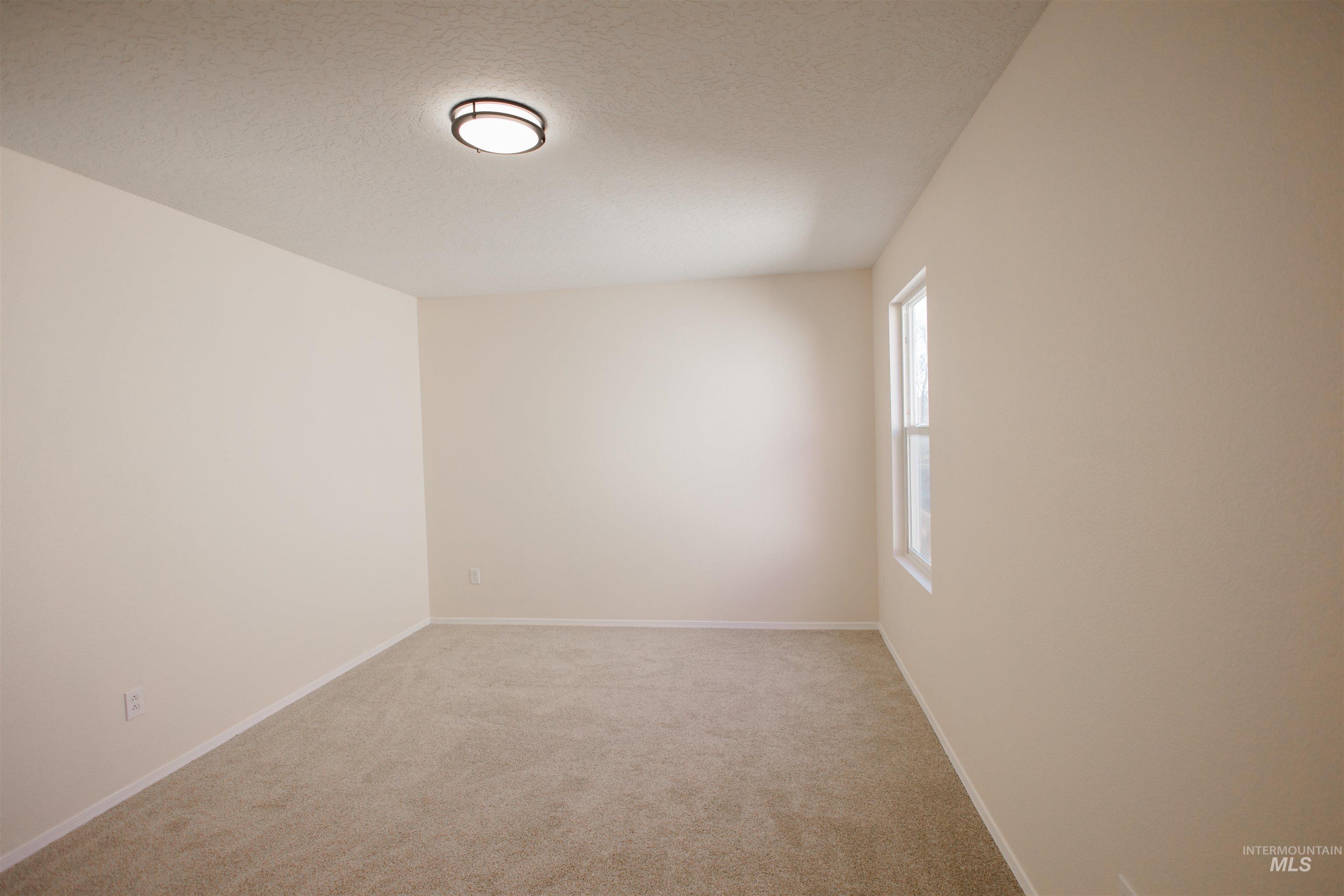 Empty room featuring light colored carpet and a textured ceiling