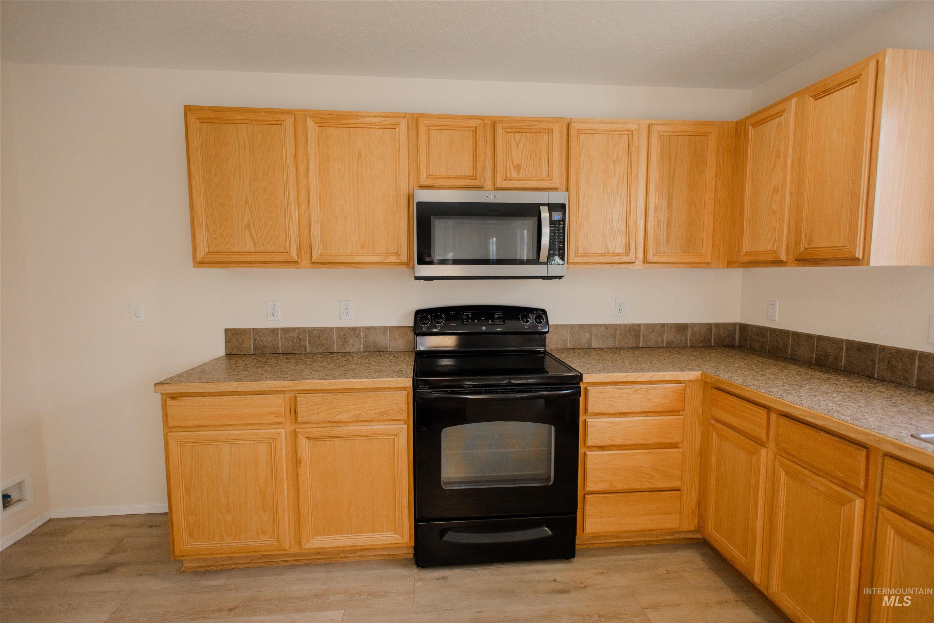 Kitchen with electric range, stainless steel microwave, light brown cabinets, and light wood finished floors