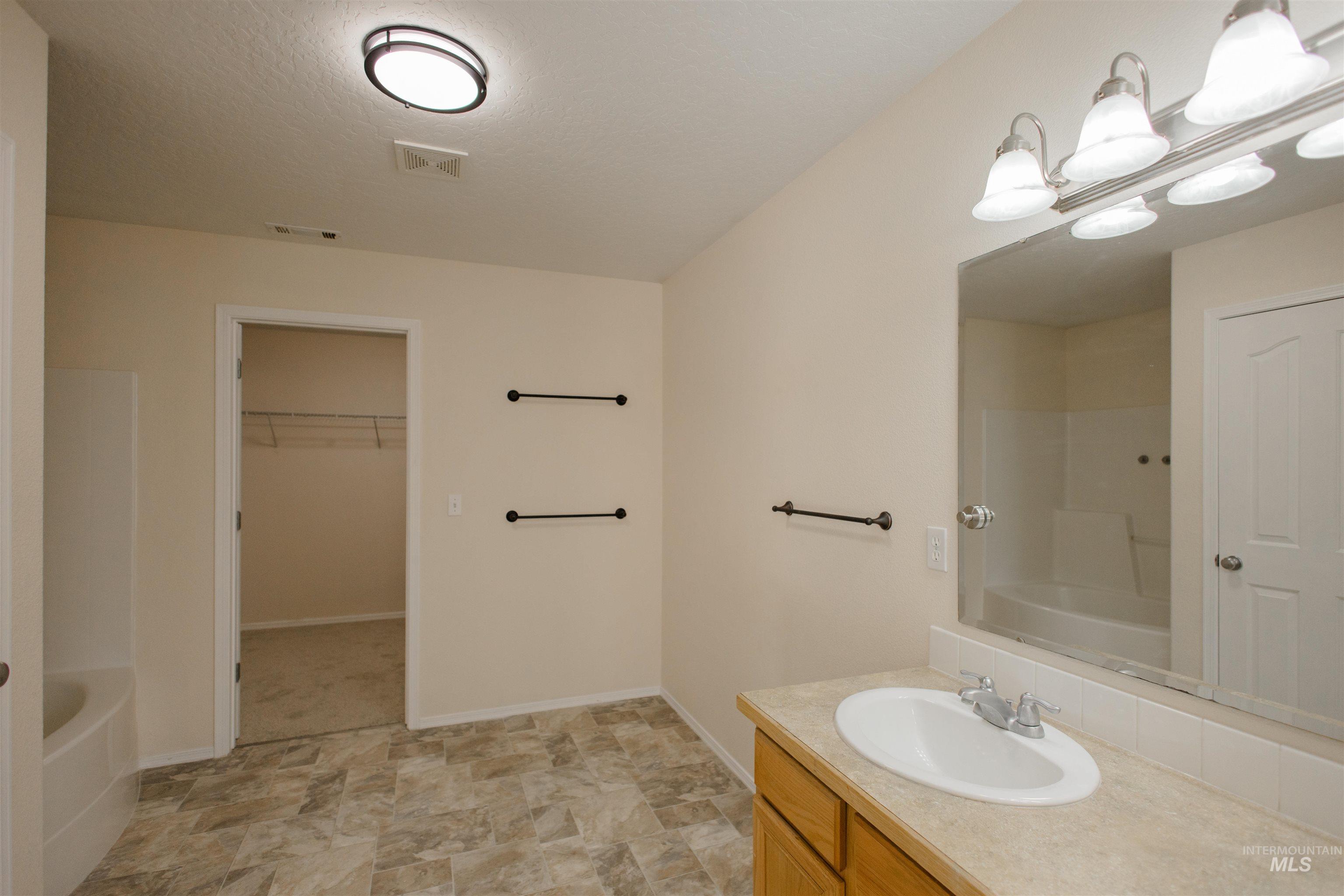 Full bathroom featuring a spacious closet, vanity, bathtub / shower combination, and a textured ceiling