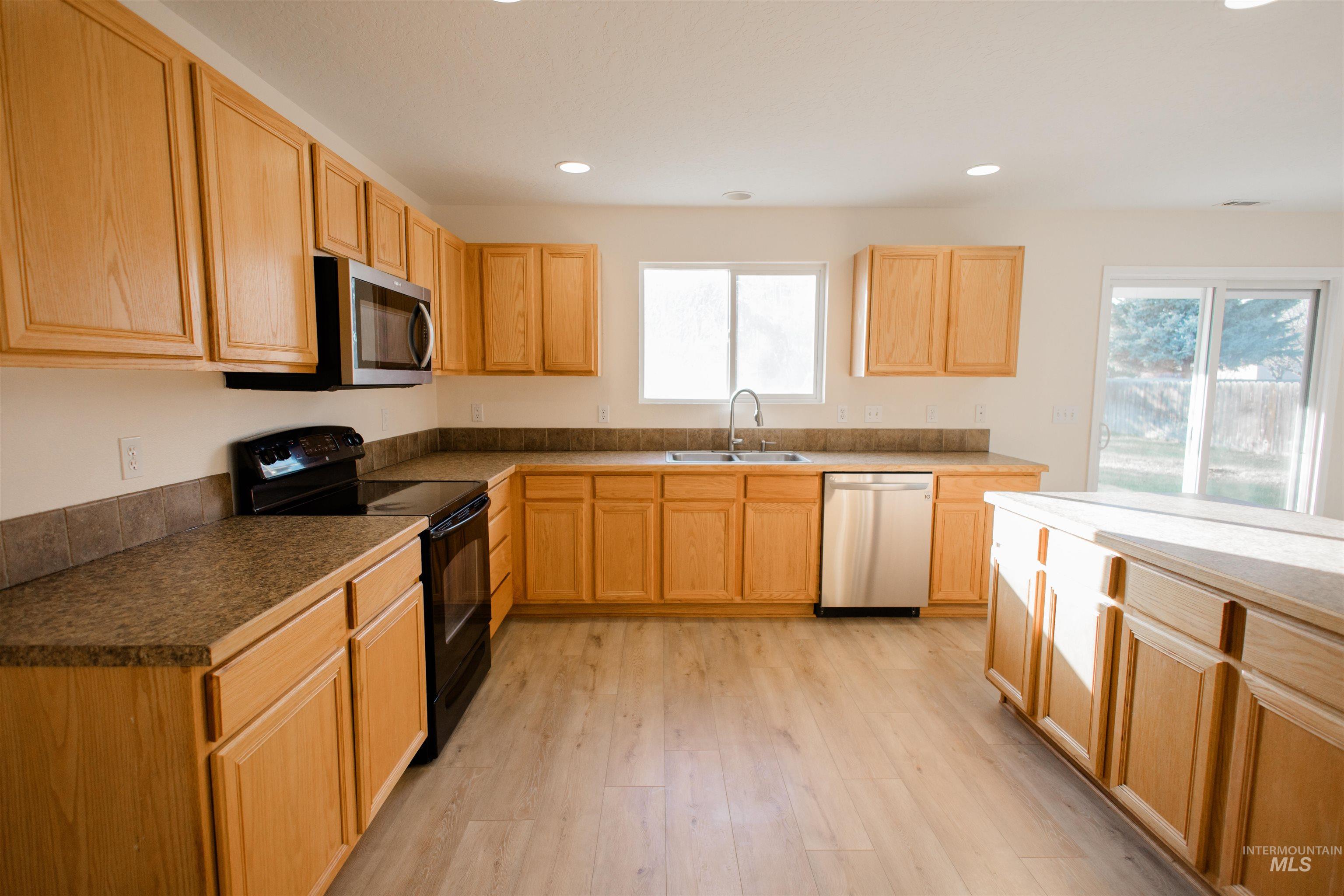 Kitchen with stainless steel appliances, light brown cabinetry, recessed lighting, light wood-style floors, and dark countertops