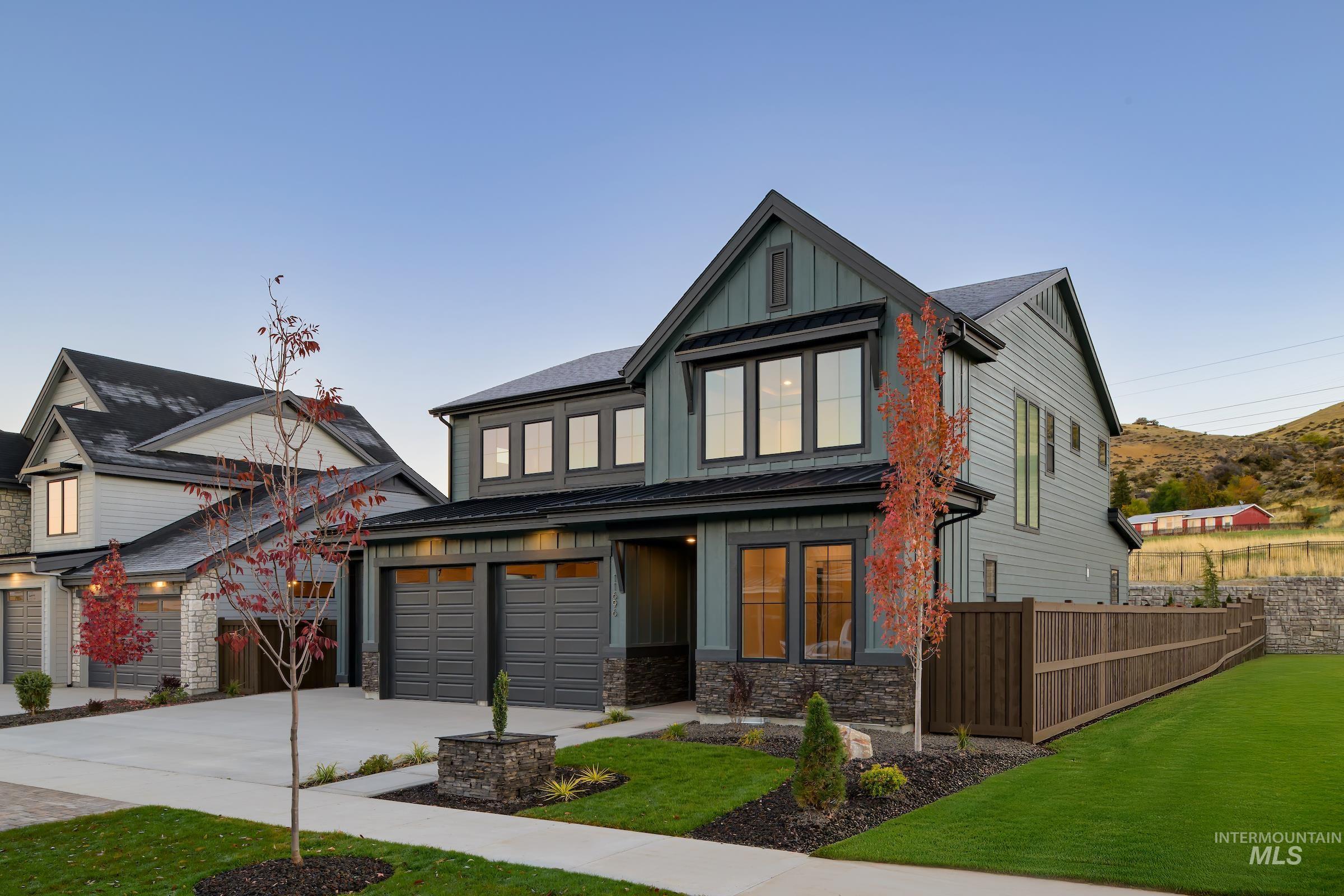 View of front of home with board and batten siding, driveway, stone siding, an attached garage, and a standing seam roof