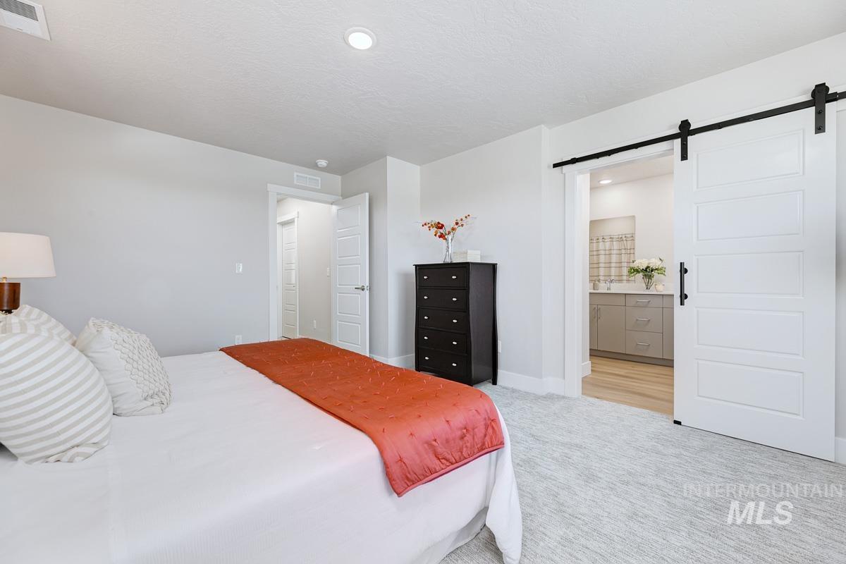 Carpeted bedroom with a barn door, ensuite bath, a textured ceiling, and recessed lighting