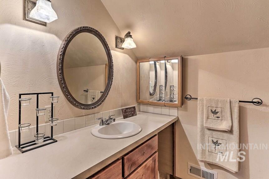 Bathroom with vanity, a textured wall, and vaulted ceiling
