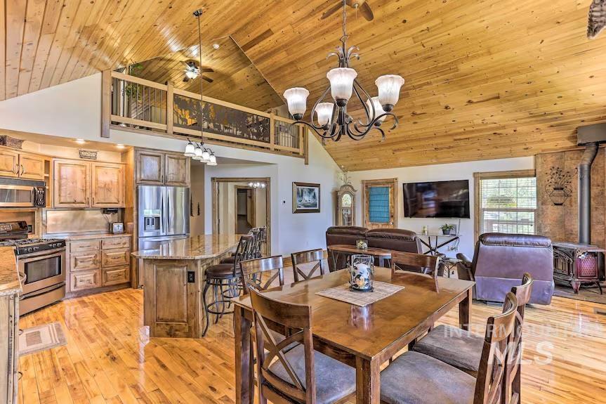 Dining room featuring a wood stove, high vaulted ceiling, wooden ceiling, light wood-style flooring, and a chandelier