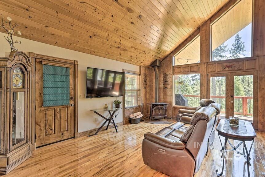 Living room with a wood stove, high vaulted ceiling, wood-type flooring, wood ceiling, and french doors