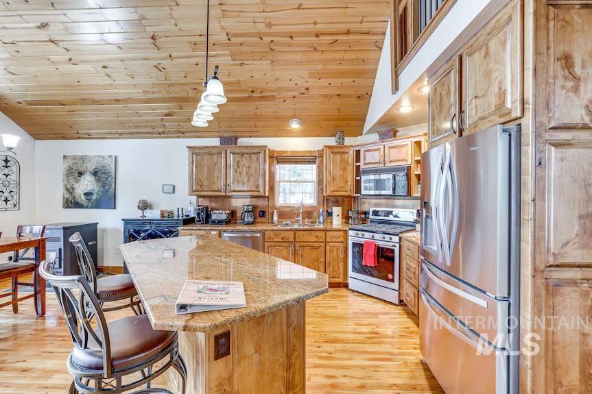 Kitchen with stainless steel appliances, light wood finished floors, a kitchen bar, lofted ceiling, and a center island