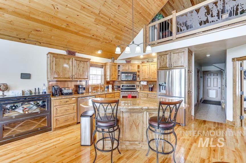 Kitchen featuring appliances with stainless steel finishes, light wood-style floors, wooden ceiling, a breakfast bar, and hanging light fixtures