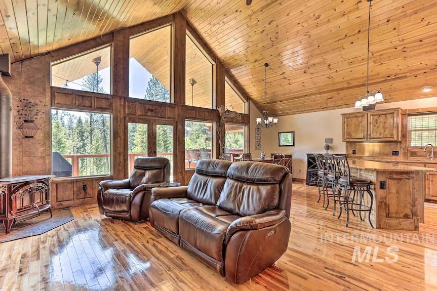 Living area with a wood stove, a chandelier, high vaulted ceiling, light wood-style floors, and wooden ceiling