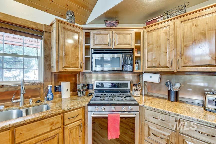 Kitchen featuring stainless steel appliances, light stone countertops, backsplash, and vaulted ceiling