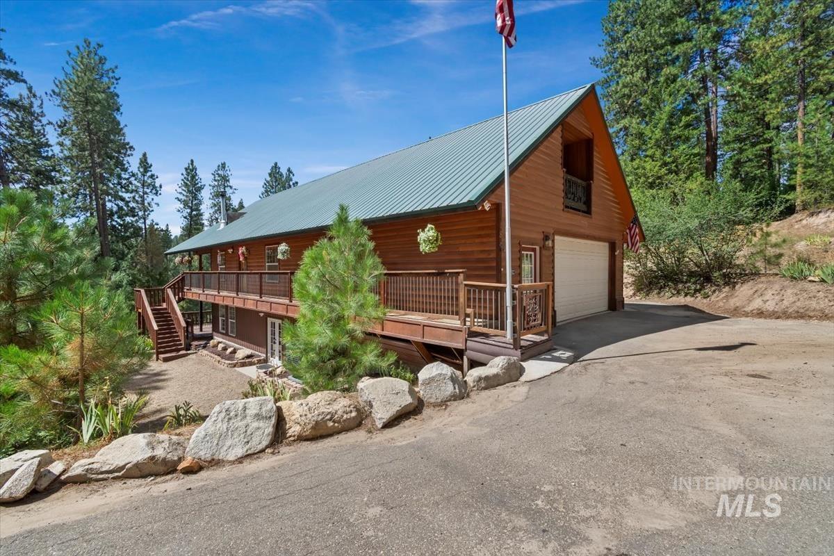 View of front of home with a wooden deck, stairs, a garage, a metal roof, and driveway
