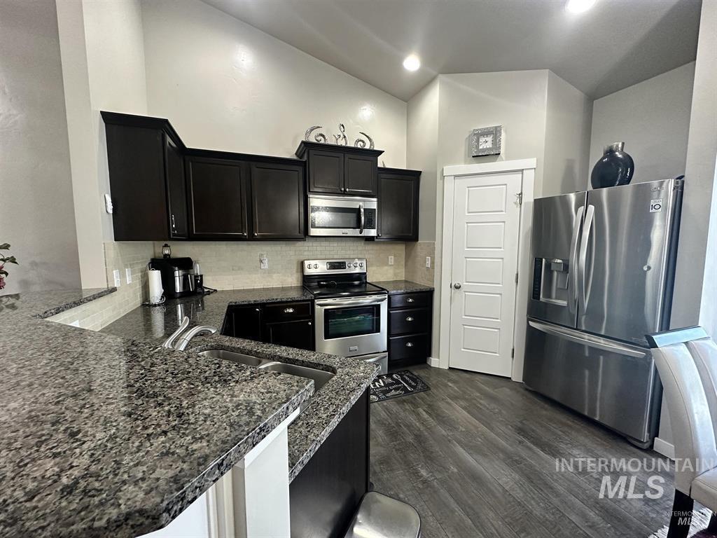 Kitchen featuring dark cabinets, stainless steel appliances, backsplash, and dark wood-type flooring