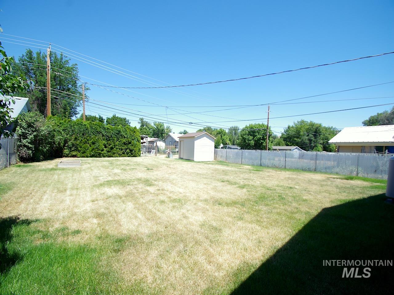 Expansive backyard featuring a chain-link fence perimeter, a detached storage shed, and mature perimeter trees