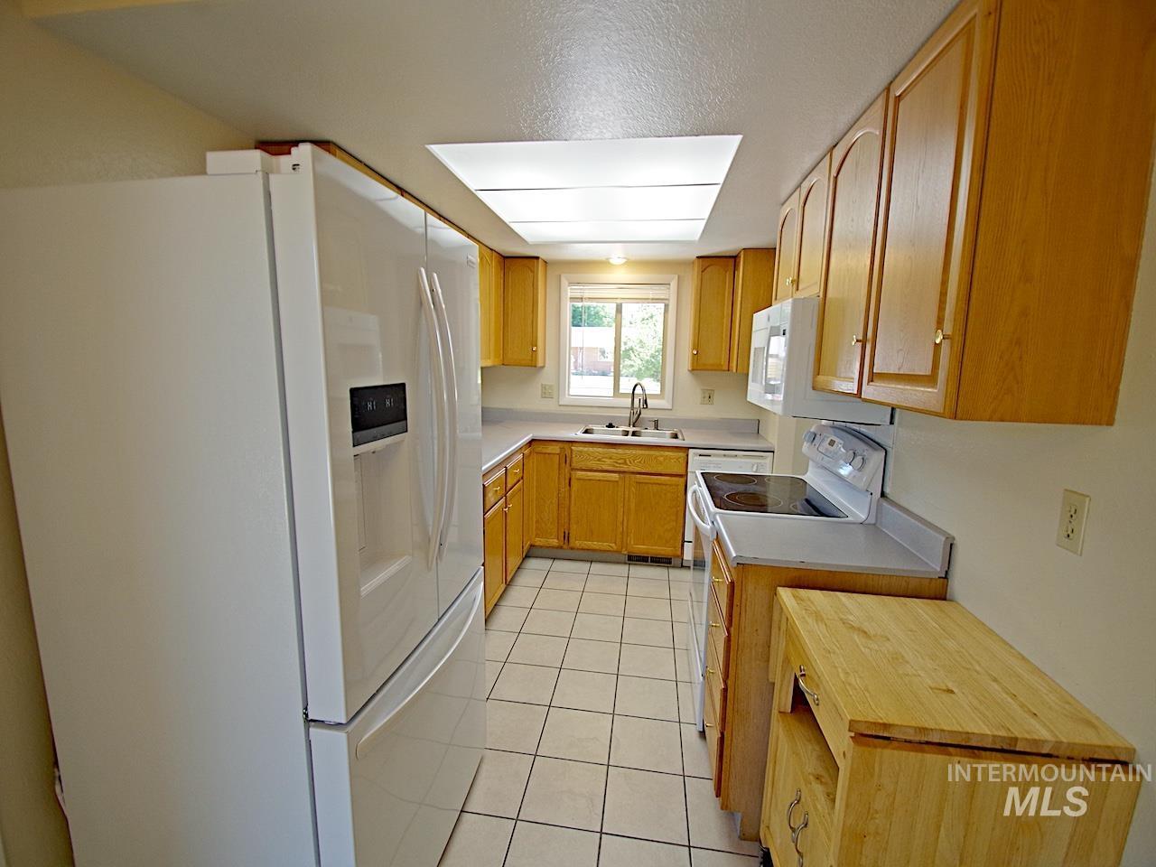 Kitchen featuring tile flooring, wood cabinetry, light-toned countertops, and a full suite of white appliances
