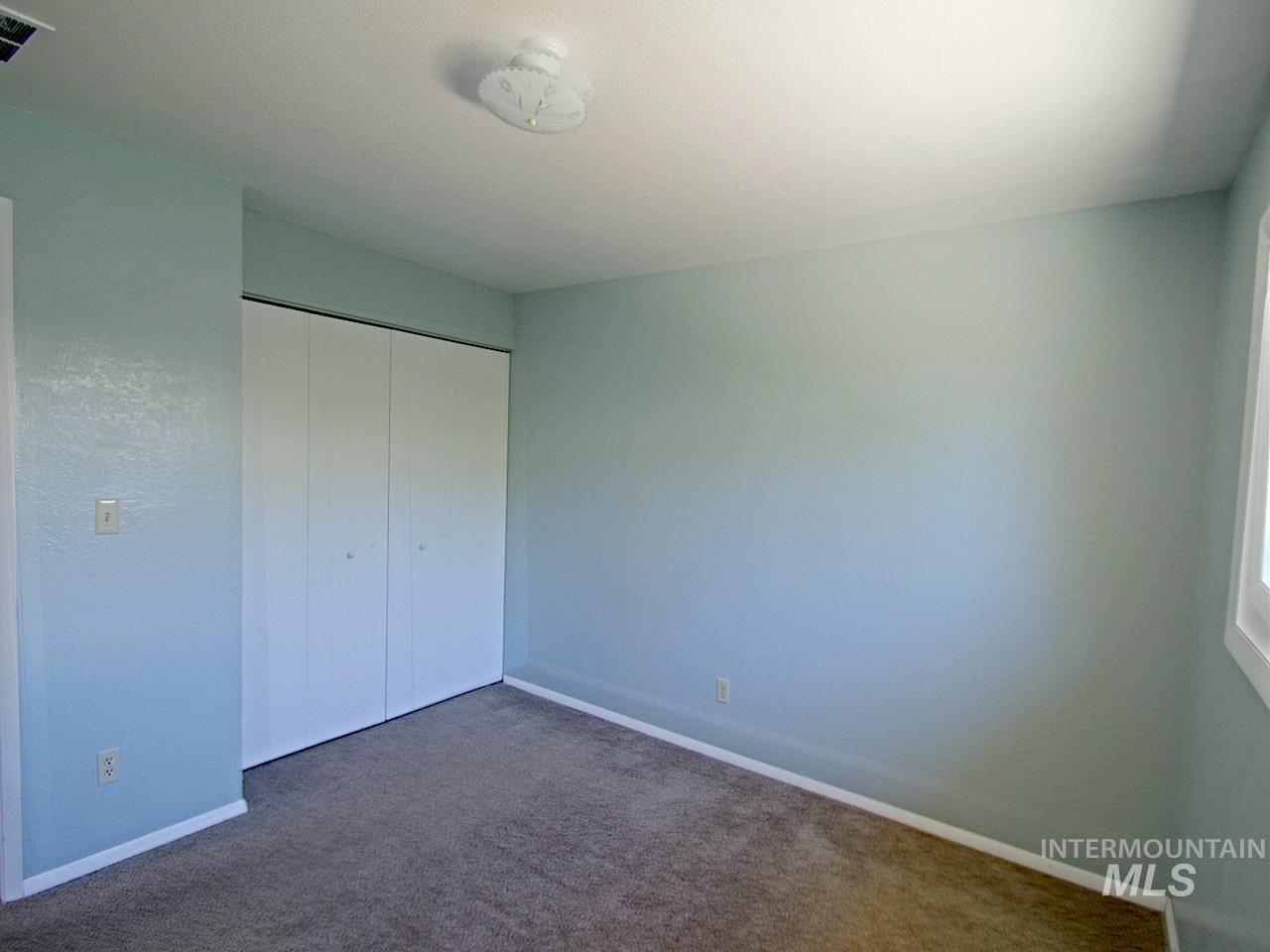 Room featuring neutral-toned carpet, light blue walls, white trim, a flush-mount ceiling light fixture, and a bi-fold closet