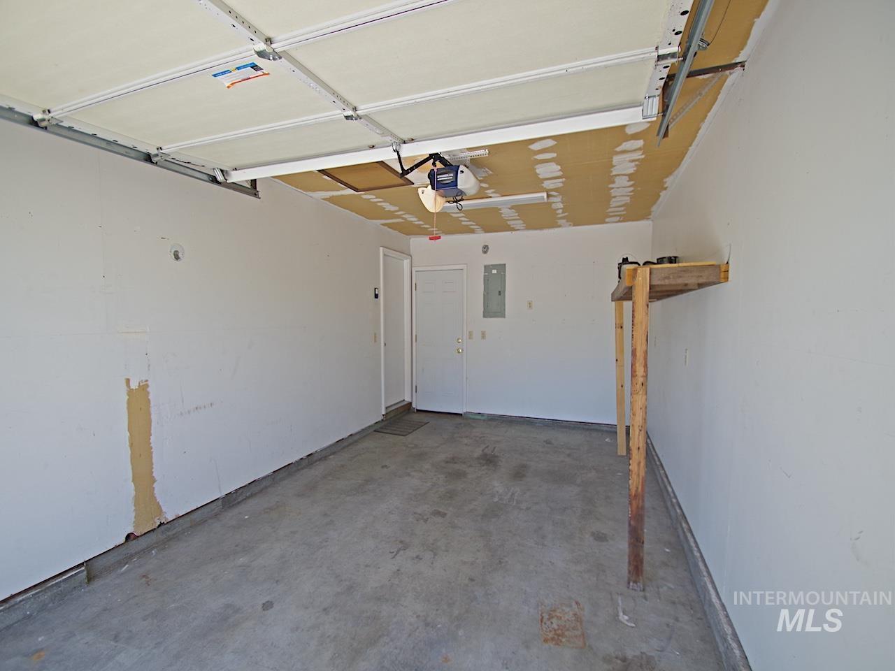 One-car garage featuring a concrete floor, built-in shelving, white walls, and an overhead garage door with opener