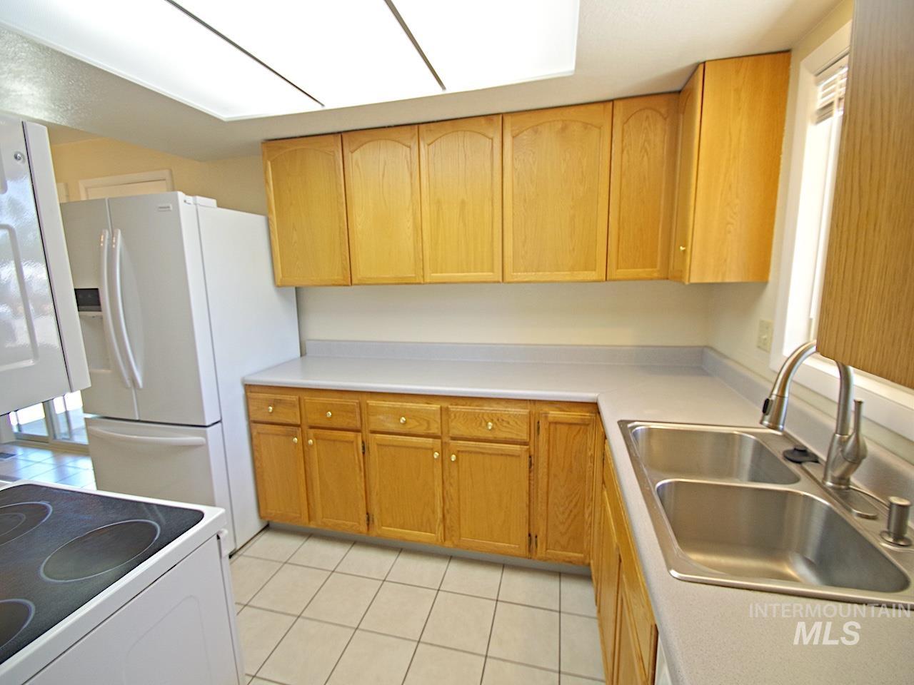 Kitchen featuring wood cabinetry, light-toned countertops, a stainless steel double basin sink with a gooseneck faucet, and white tile flooring