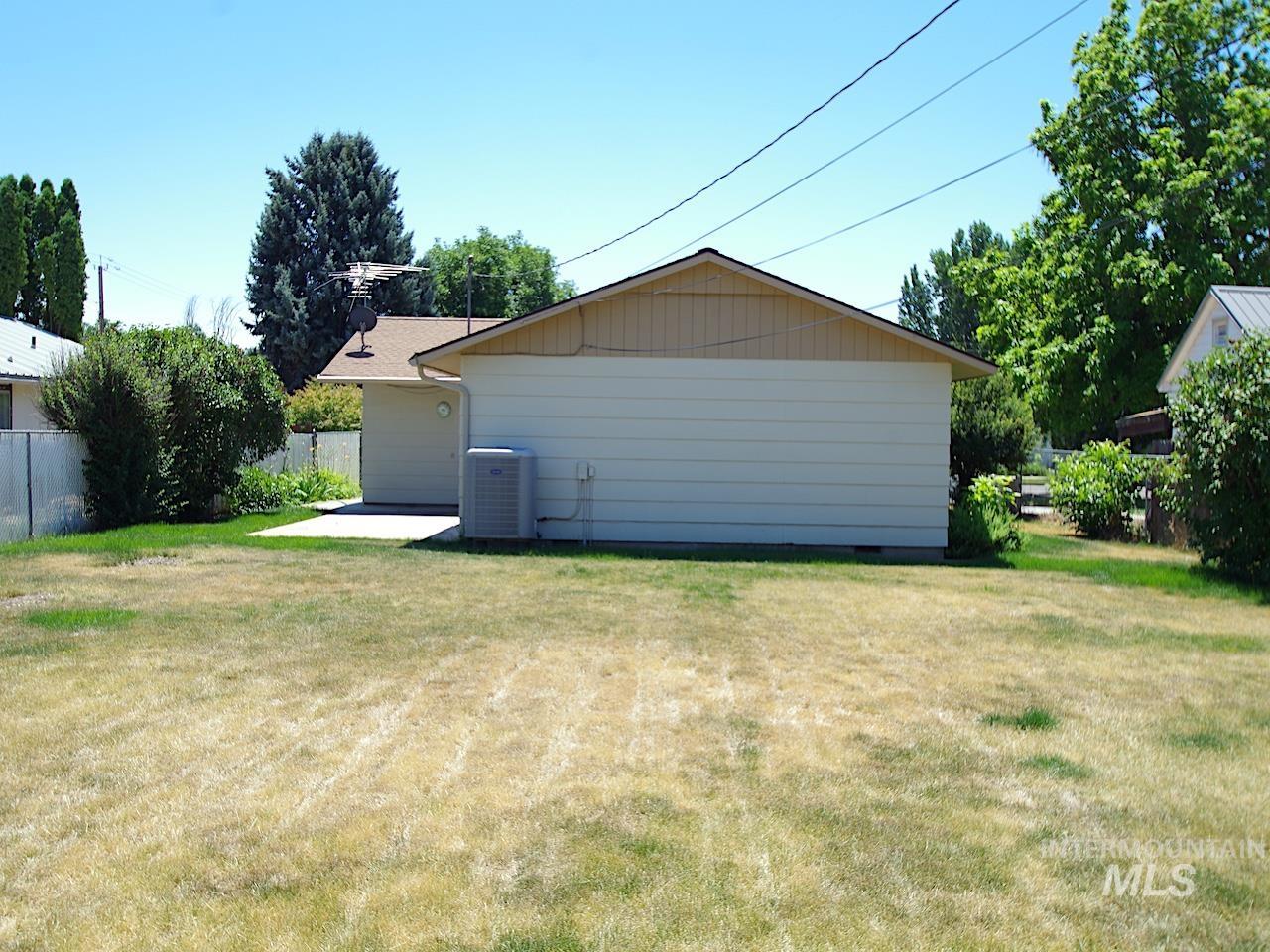 Expansive rear yard featuring a concrete patio pad, mature perimeter landscaping, and a central air conditioning unit