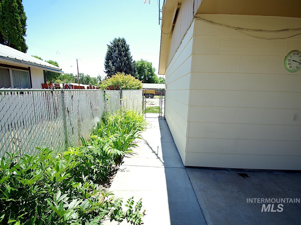 Concrete walkway alongside the property, featuring a chain-link fence with established plantings