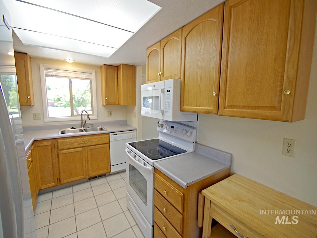 Kitchen featuring wood-finish cabinetry, light-toned countertops, and a white tile floor