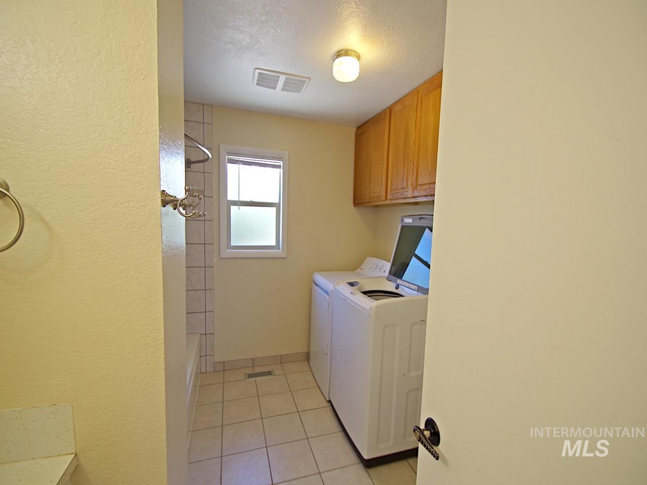 Compact laundry area featuring tile flooring, wood cabinetry, and a frosted window