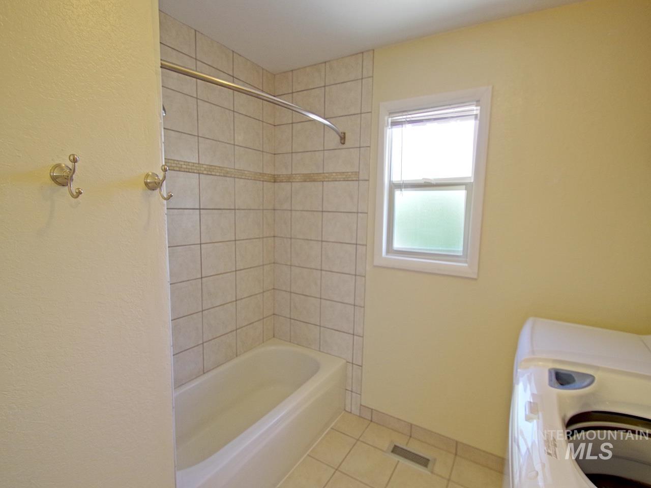 Full bathtub with tile surround, decorative accent tile band, and a shower curtain rod