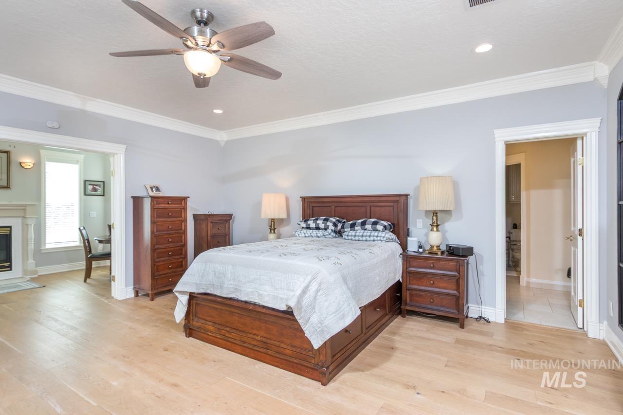 Bedroom with light wood-style floors, ornamental molding, a premium fireplace, a ceiling fan, and recessed lighting
