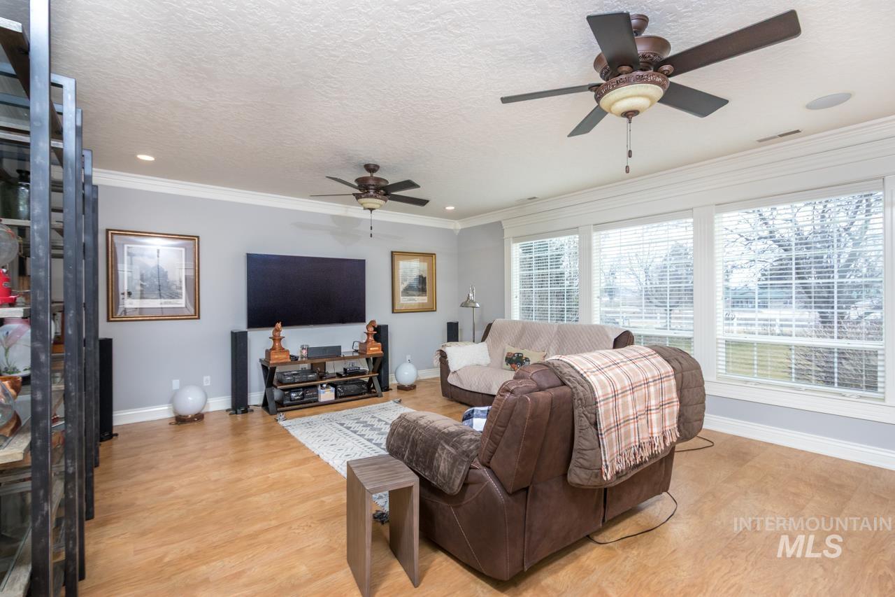 Living room featuring a ceiling fan, light wood-type flooring, a textured ceiling, ornamental molding, and recessed lighting