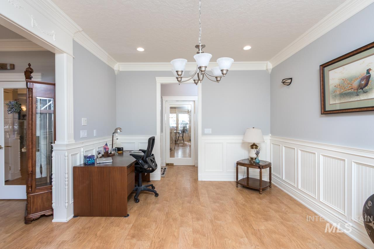 Office space featuring a wainscoted wall, suspended lighting, crown molding, light wood-style floors, and a decorative wall