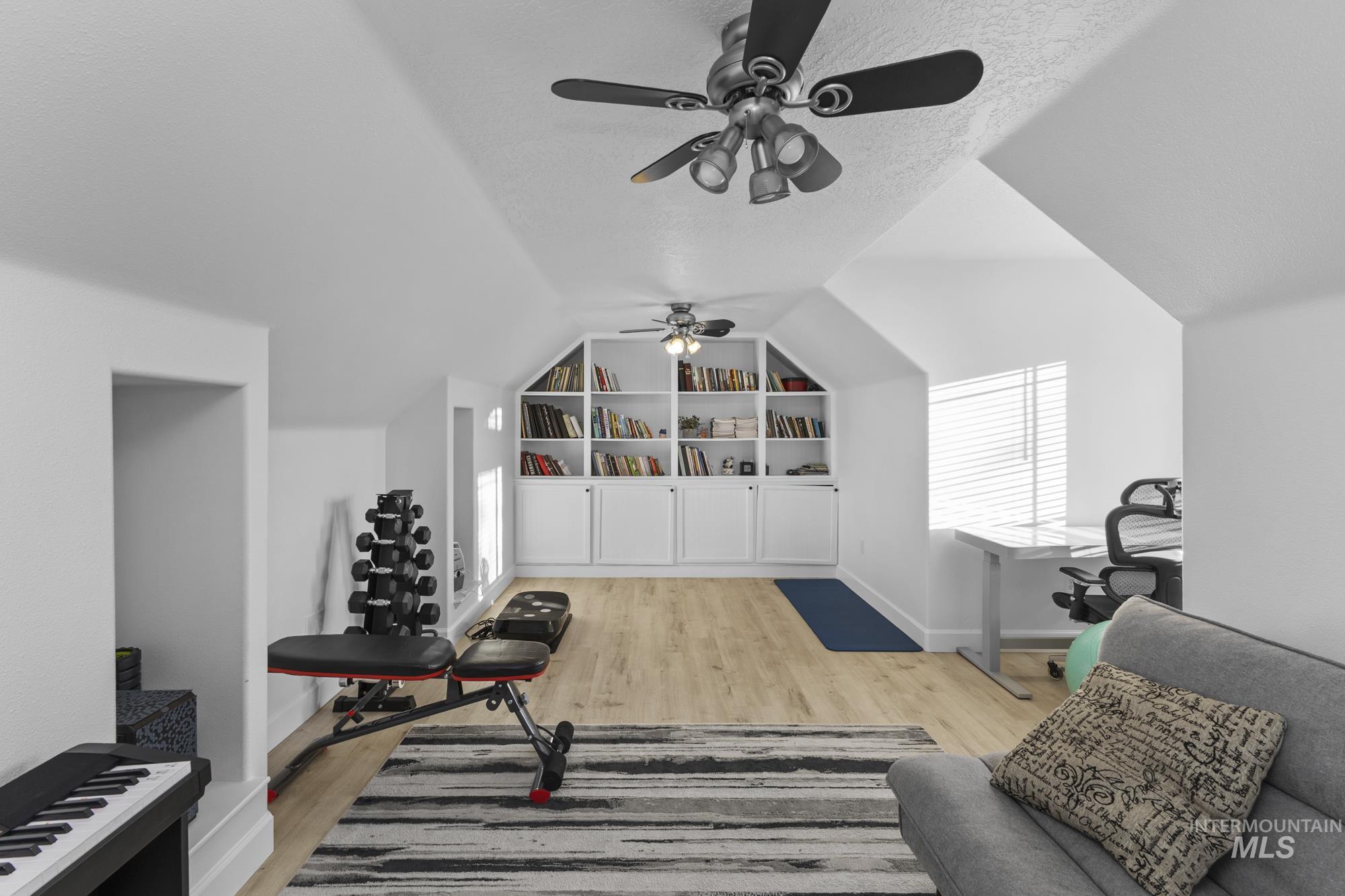 Workout room with vaulted ceiling, light wood-style flooring, a textured ceiling, and a ceiling fan