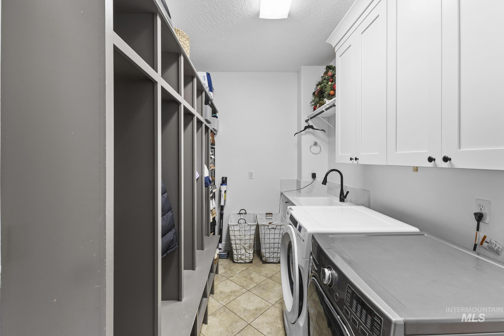 Laundry room featuring cabinet space, a textured ceiling, washing machine and clothes dryer, and light tile patterned floors