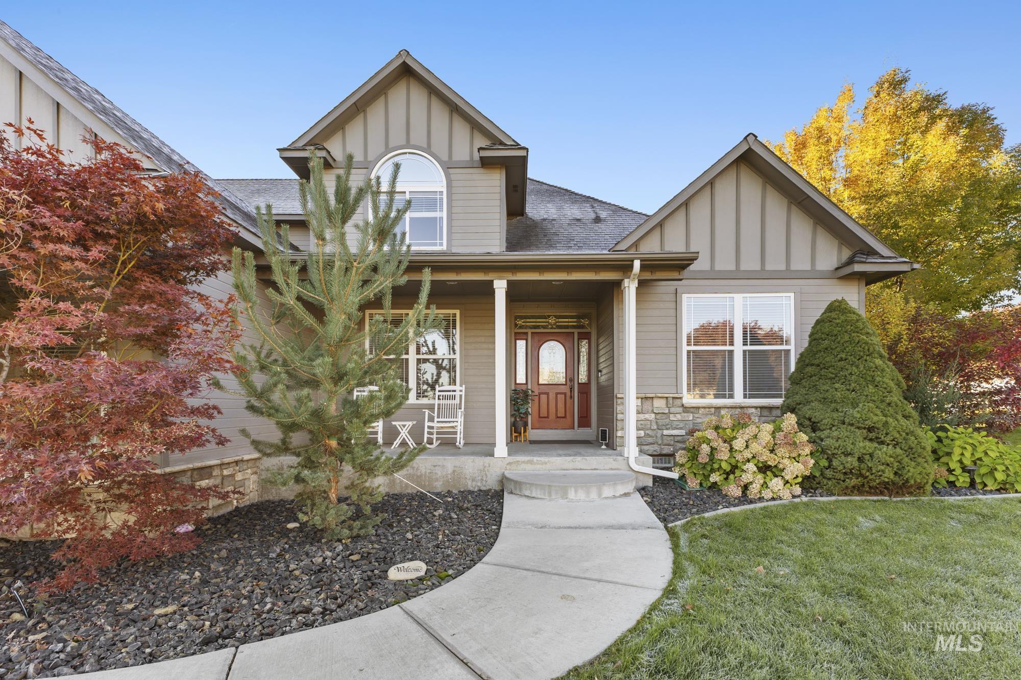 View of front of house featuring board and batten siding, stone siding, a front yard, roof with shingles, and a porch