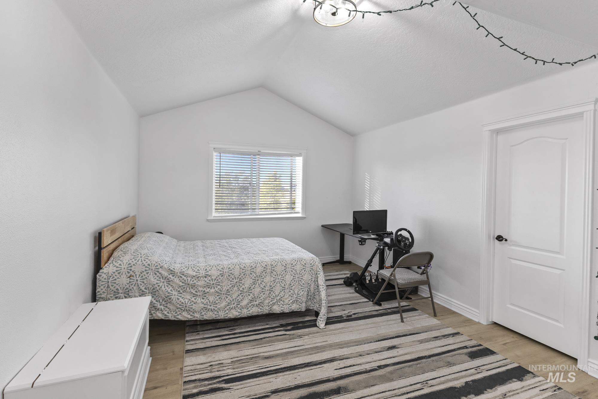 Bedroom with lofted ceiling, light wood-style floors, and a textured ceiling
