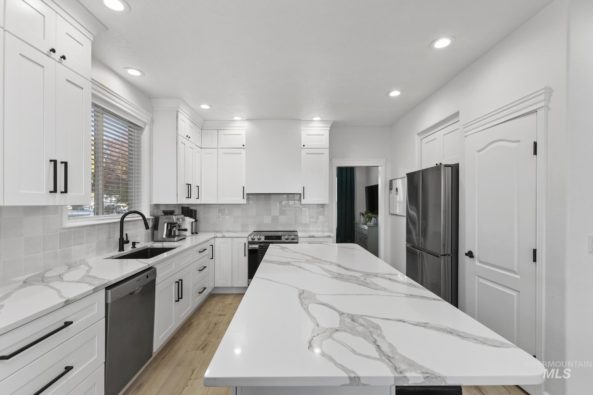 Kitchen featuring a kitchen island, light stone countertops, appliances with stainless steel finishes, light wood-type flooring, and white cabinets