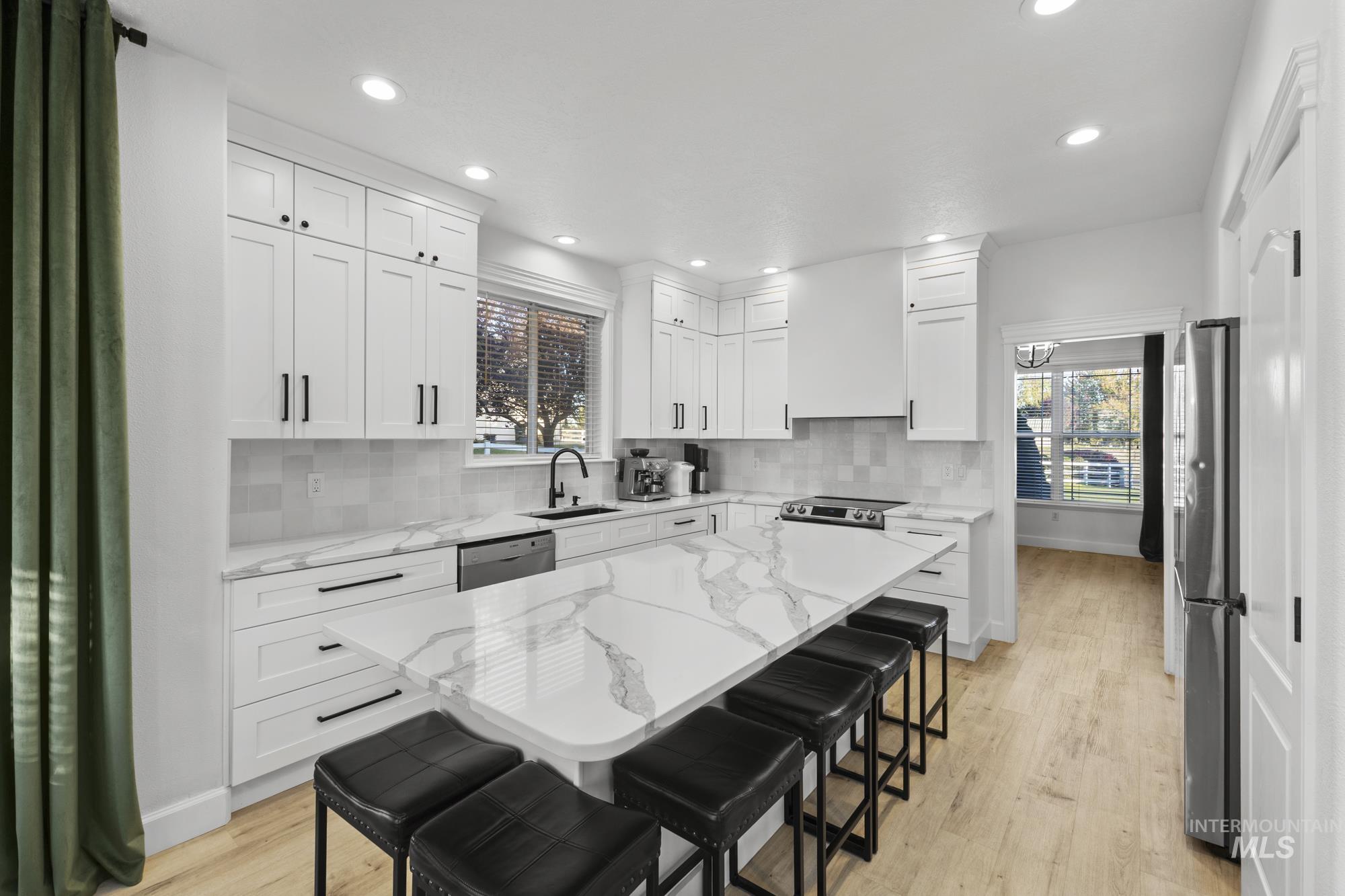 Kitchen featuring a breakfast bar area, white cabinets, light stone countertops, decorative backsplash, and recessed lighting
