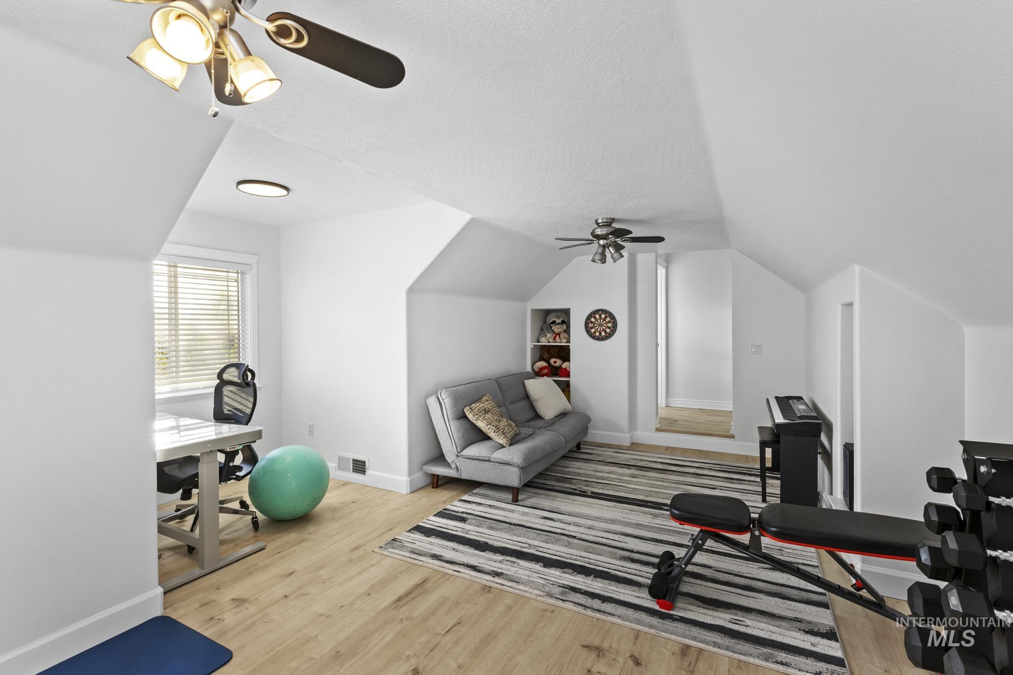 Exercise room with light wood-style flooring, a ceiling fan, vaulted ceiling, and a textured ceiling