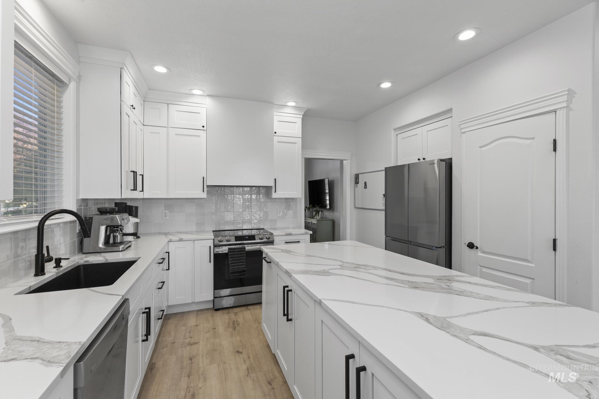 Kitchen with light stone countertops, stainless steel appliances, light wood finished floors, white cabinets, and recessed lighting