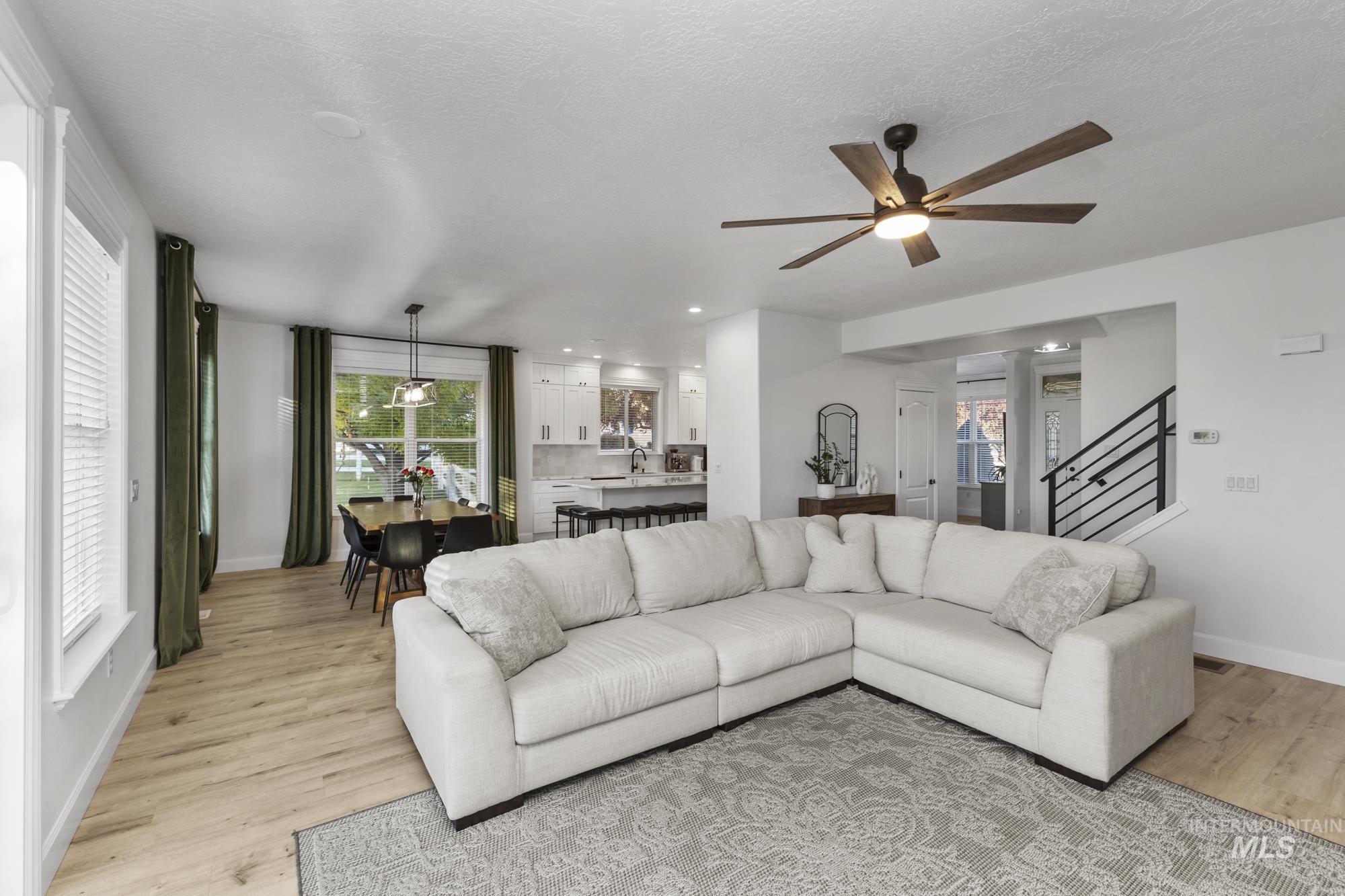 Living area featuring healthy amount of natural light, light wood-style floors, stairs, a ceiling fan, and a textured ceiling
