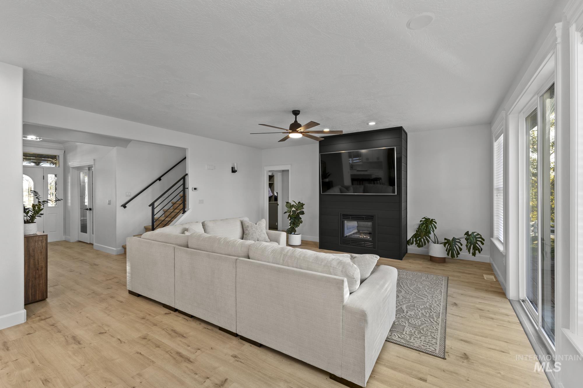 Living area with light wood-style floors, a fireplace, a ceiling fan, stairs, and recessed lighting