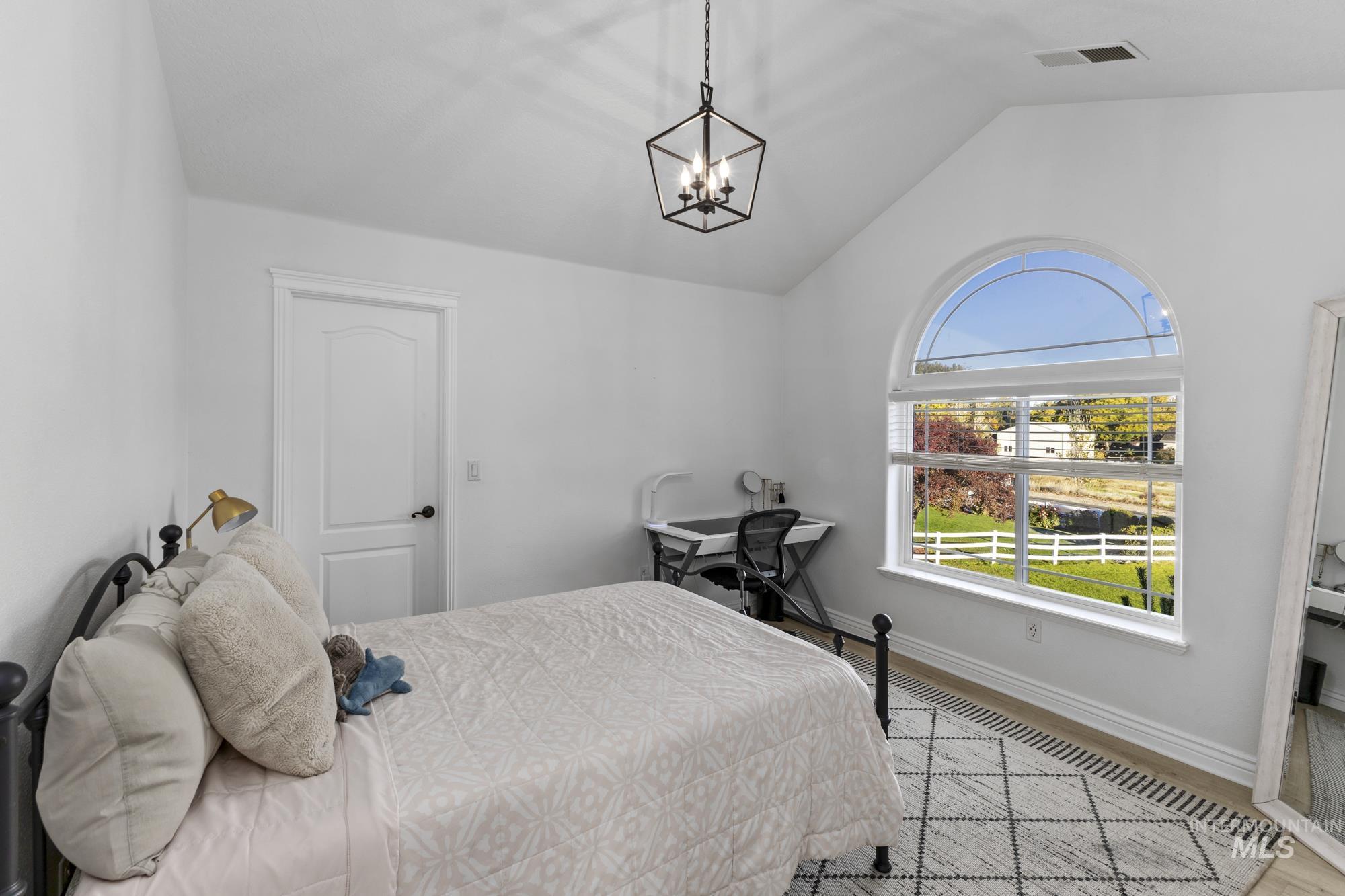 Bedroom with vaulted ceiling, light wood finished floors, and a chandelier