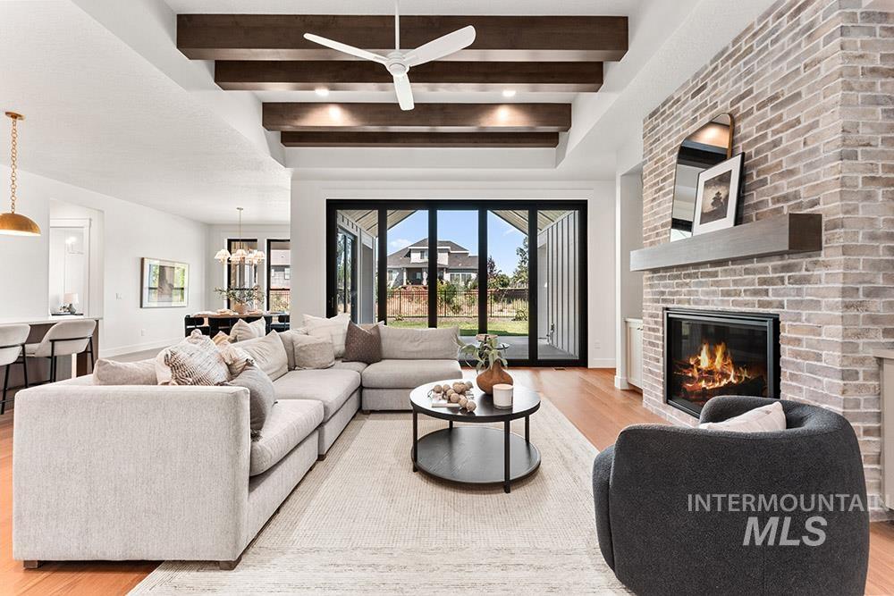 Living room with light wood finished floors, beamed ceiling, a fireplace, ceiling fan, and a chandelier