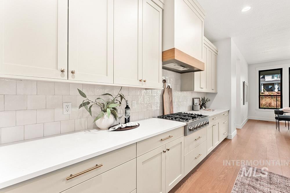 Kitchen featuring light wood finished floors, stainless steel gas cooktop, backsplash, white cabinets, and premium range hood
