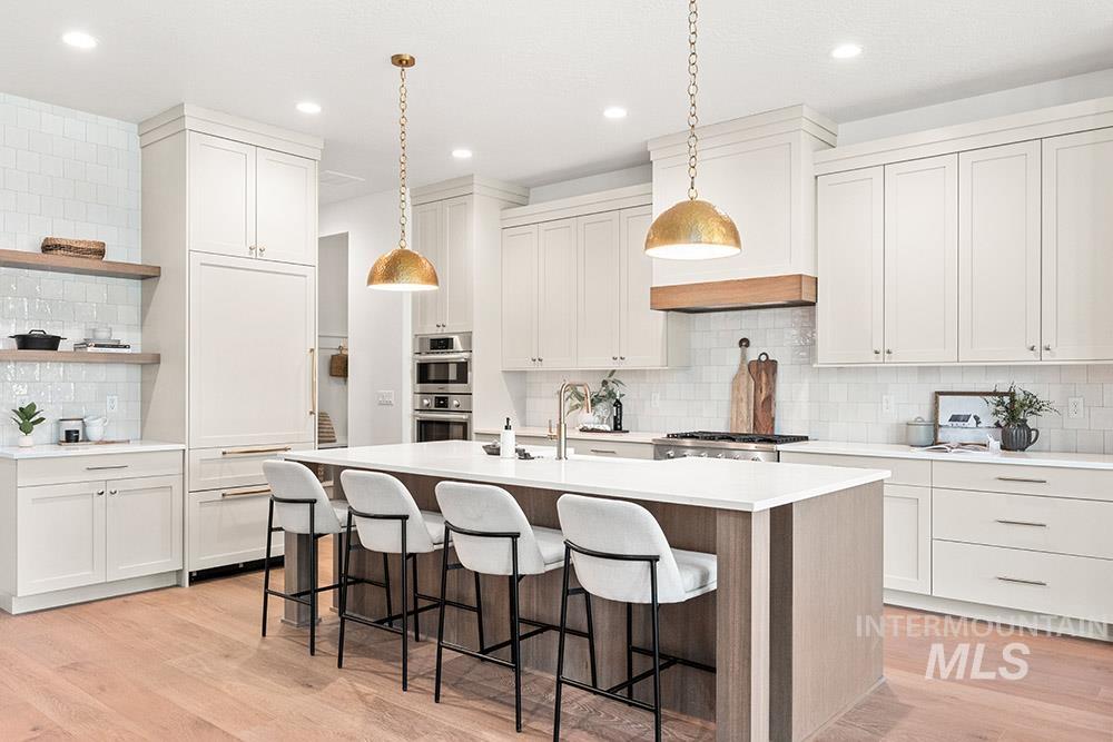 Kitchen with decorative backsplash, white cabinetry, light wood-type flooring, a center island with sink, and open shelves