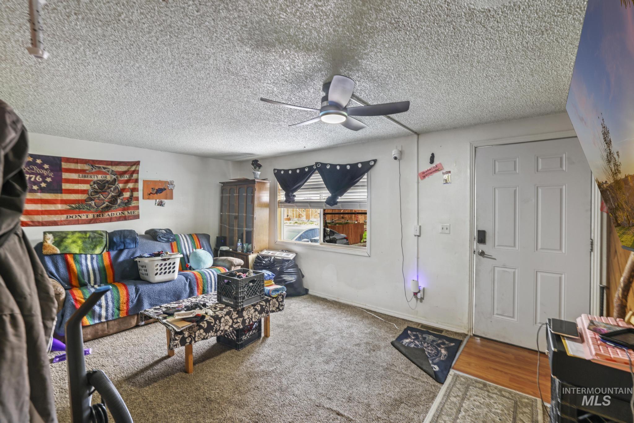 Carpeted living area featuring a textured ceiling, ceiling fan, and wood finished floors