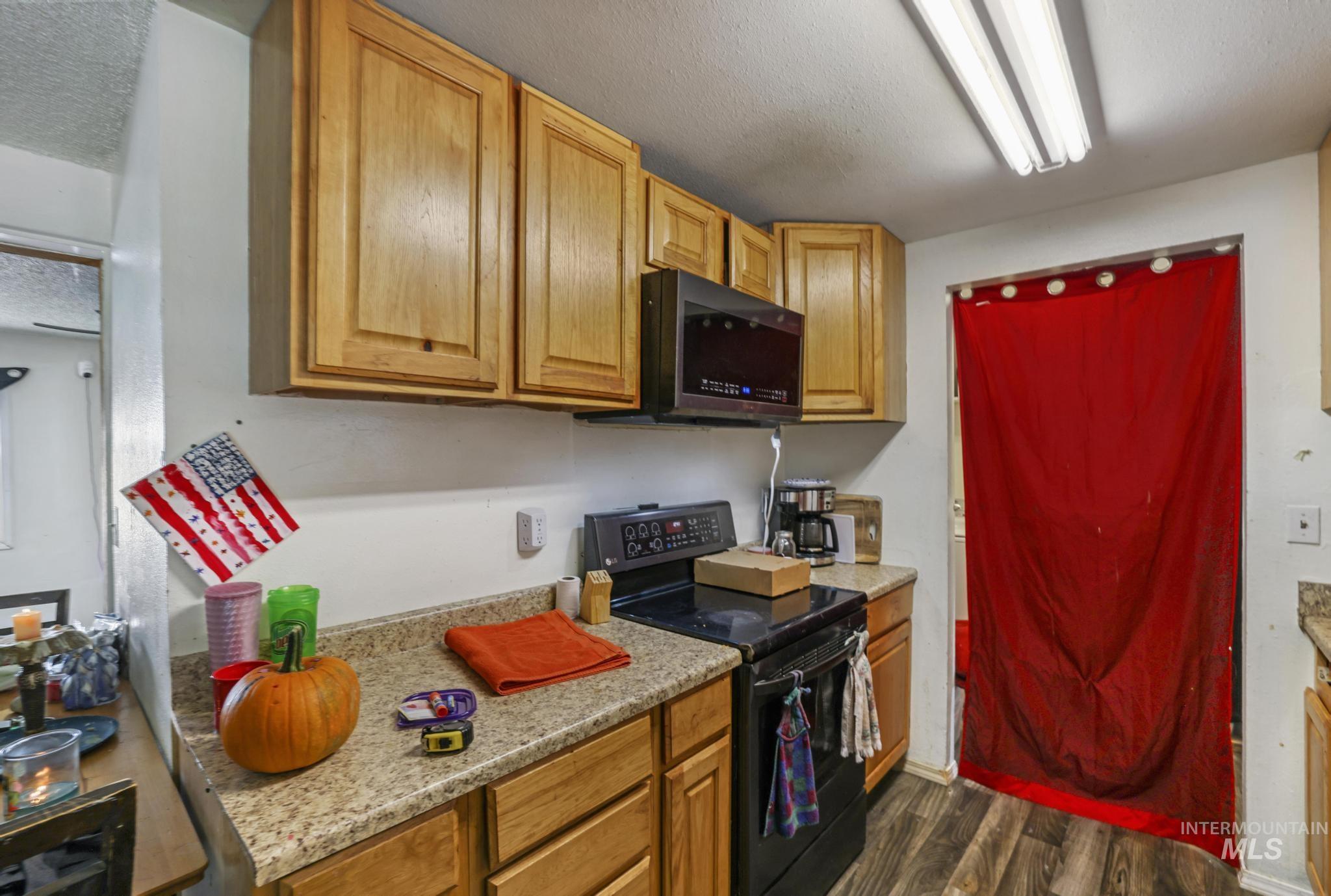 Kitchen featuring black electric range oven, dark wood finished floors, a textured ceiling, and brown cabinets