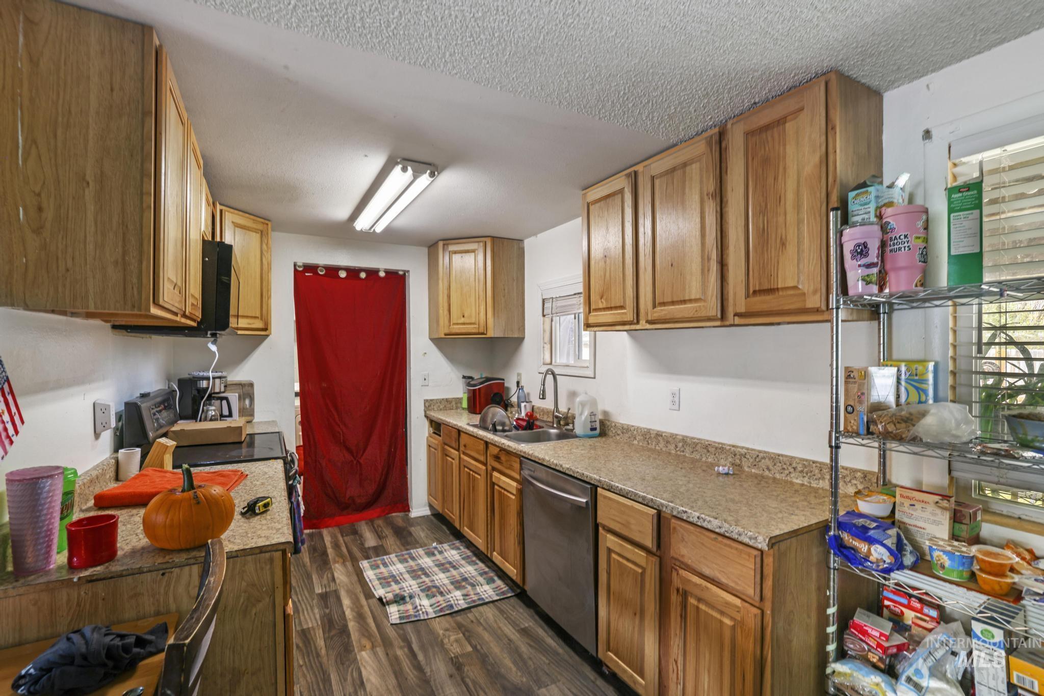 Kitchen featuring dark wood-style flooring, electric range oven, dishwasher, brown cabinetry, and a textured ceiling
