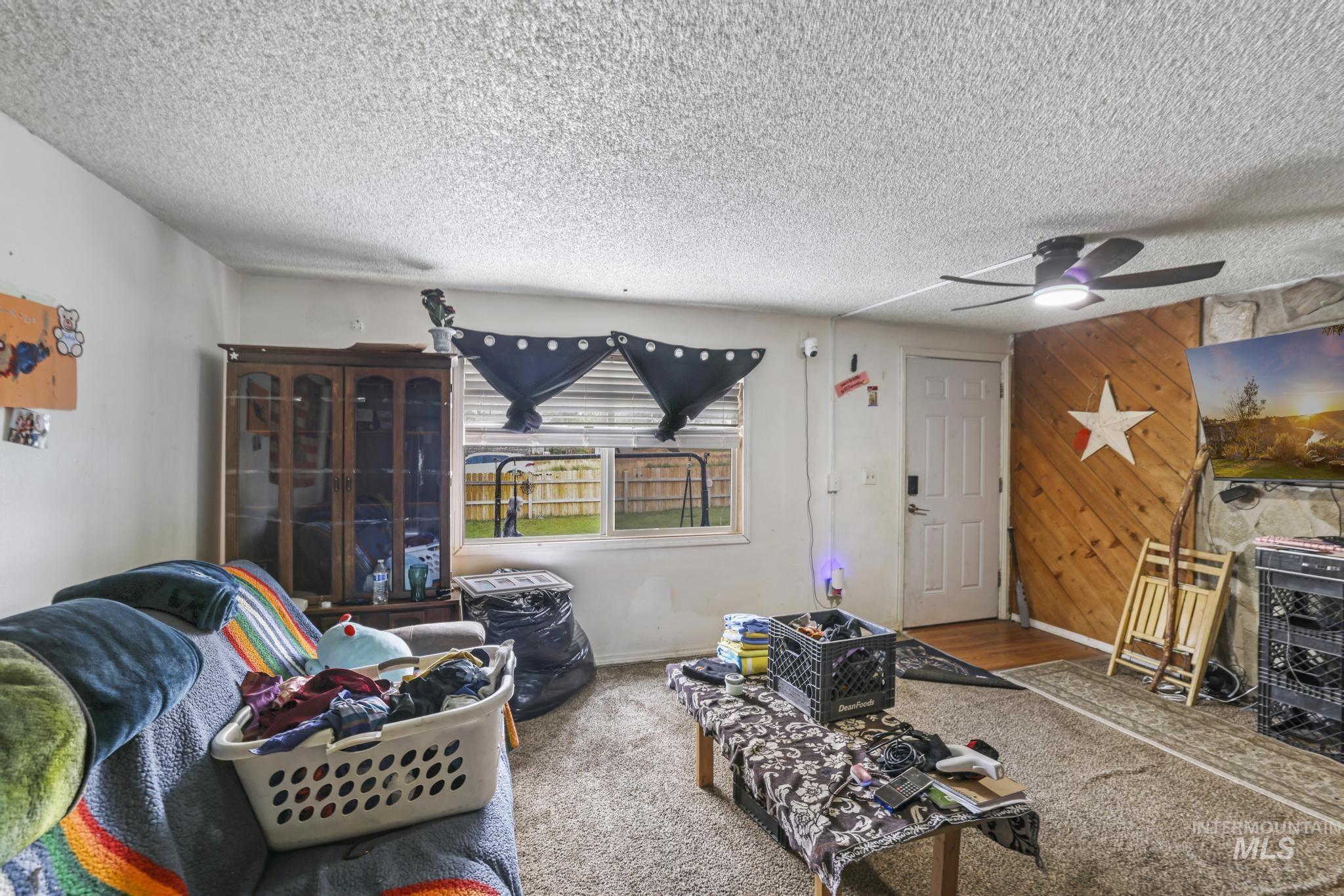 Living room with a textured ceiling, wooden walls, carpet, and a ceiling fan