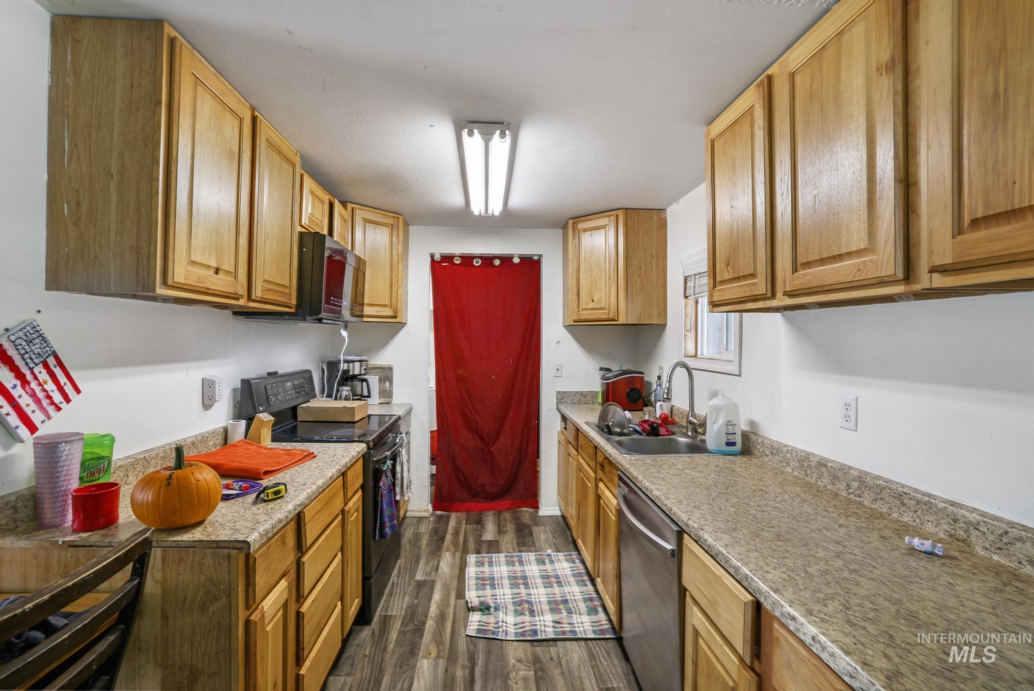 Kitchen with black electric range, dark wood finished floors, stainless steel dishwasher, and brown cabinets