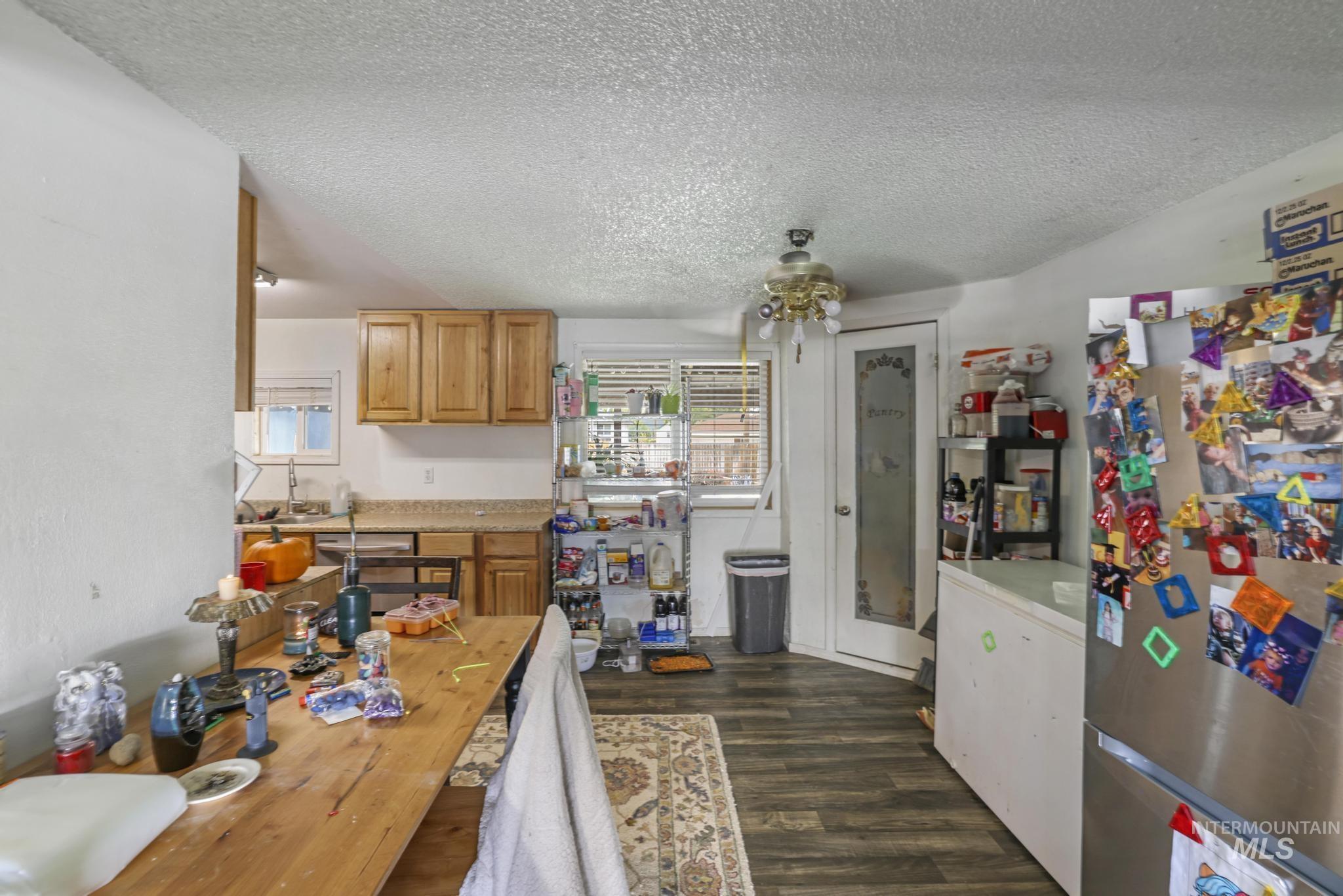 Kitchen featuring freestanding refrigerator, dark wood-style flooring, a textured ceiling, white refrigerator, and brown cabinetry