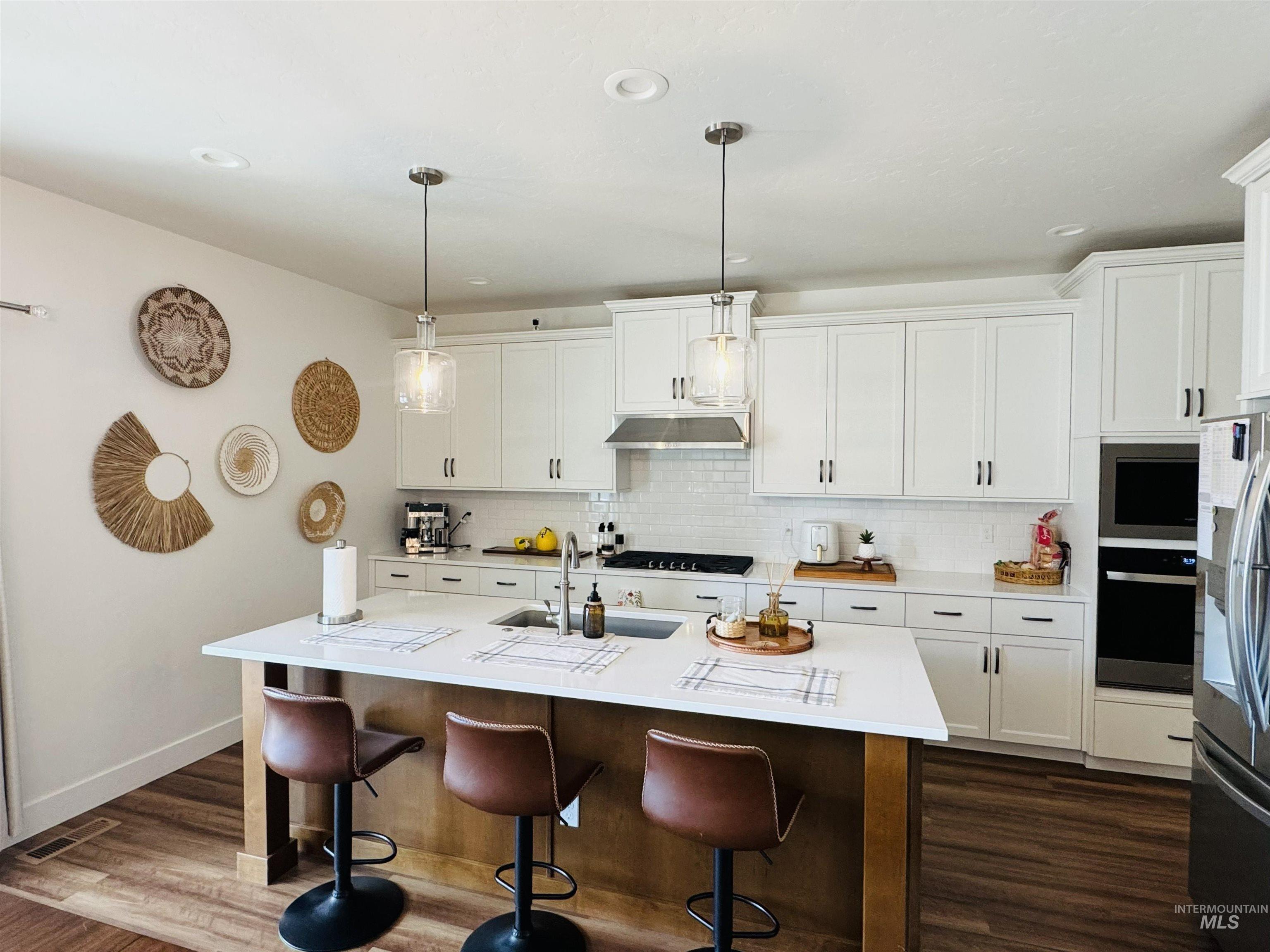 Two tone kitchen with a breakfast bar area, a kitchen island with sink, stainless steel appliances, decorative light fixtures, and dual tone cabinets
