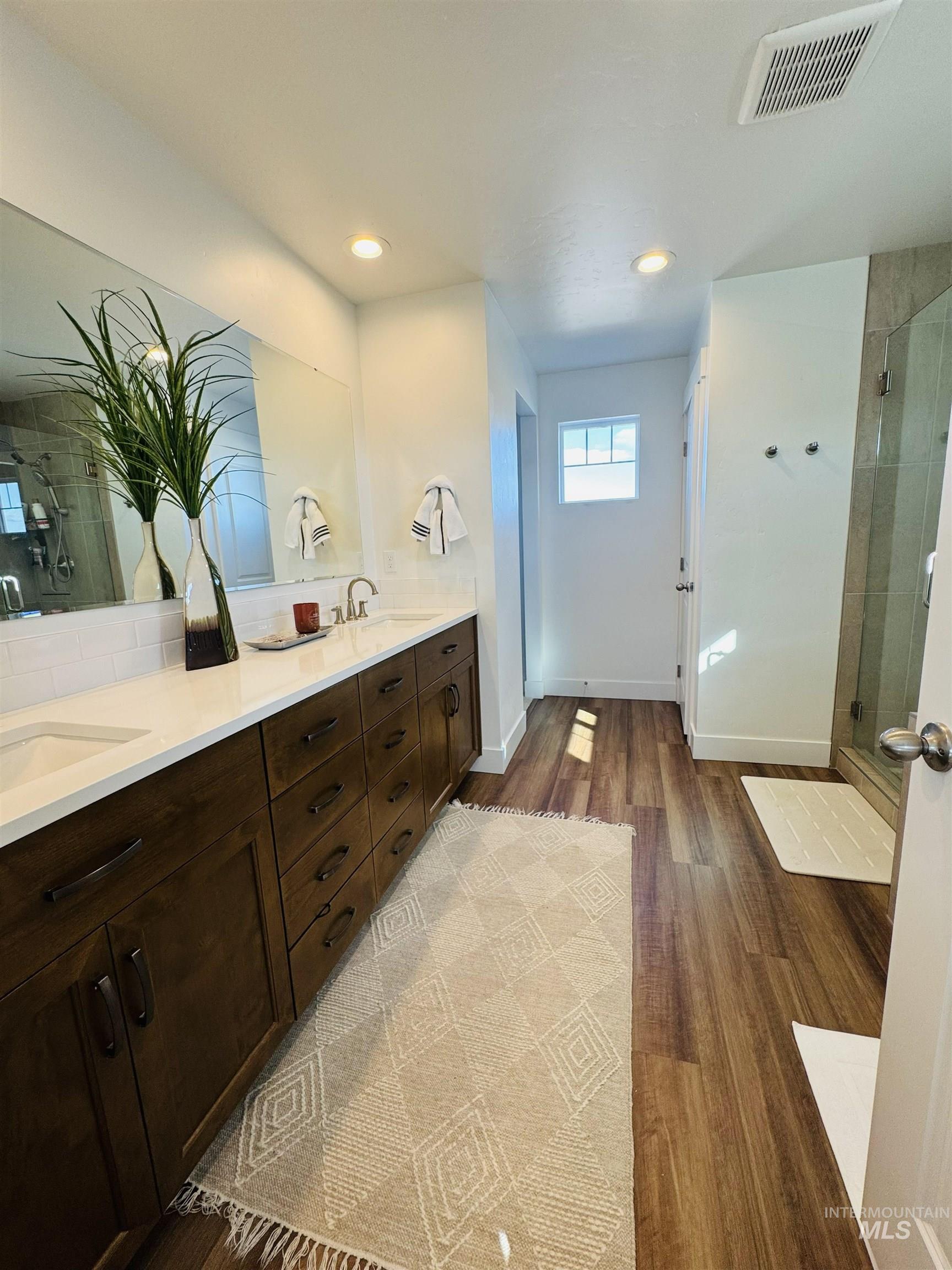 Full bathroom featuring a shower stall, double vanity, dark wood-style floors, and recessed lighting